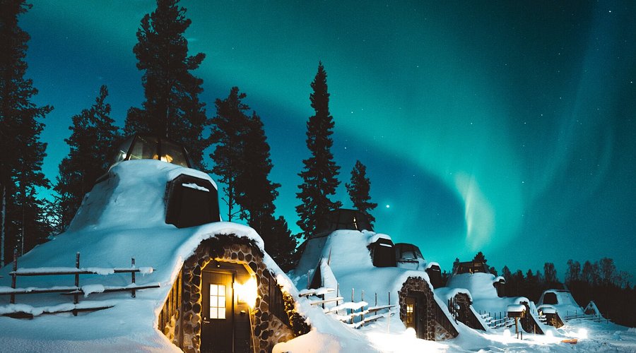 Snow-covered glass-roofed cabins under the northern lights.