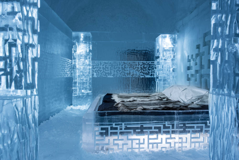 An ice bedroom with a carved ice bed, fur covers and blue light.