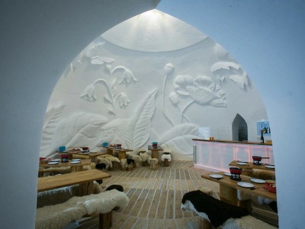 A snow dining dome with carved walls, wooden tables and fur-covered benches.